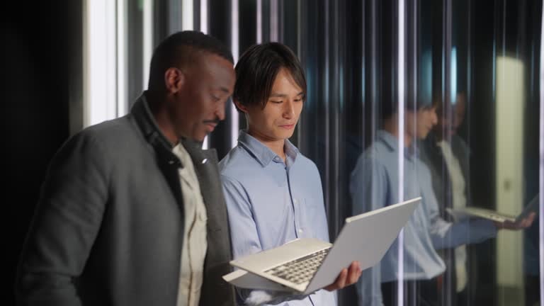 two-multi-ethnic-businessmen-using-laptop-while-on-the-move-in-office